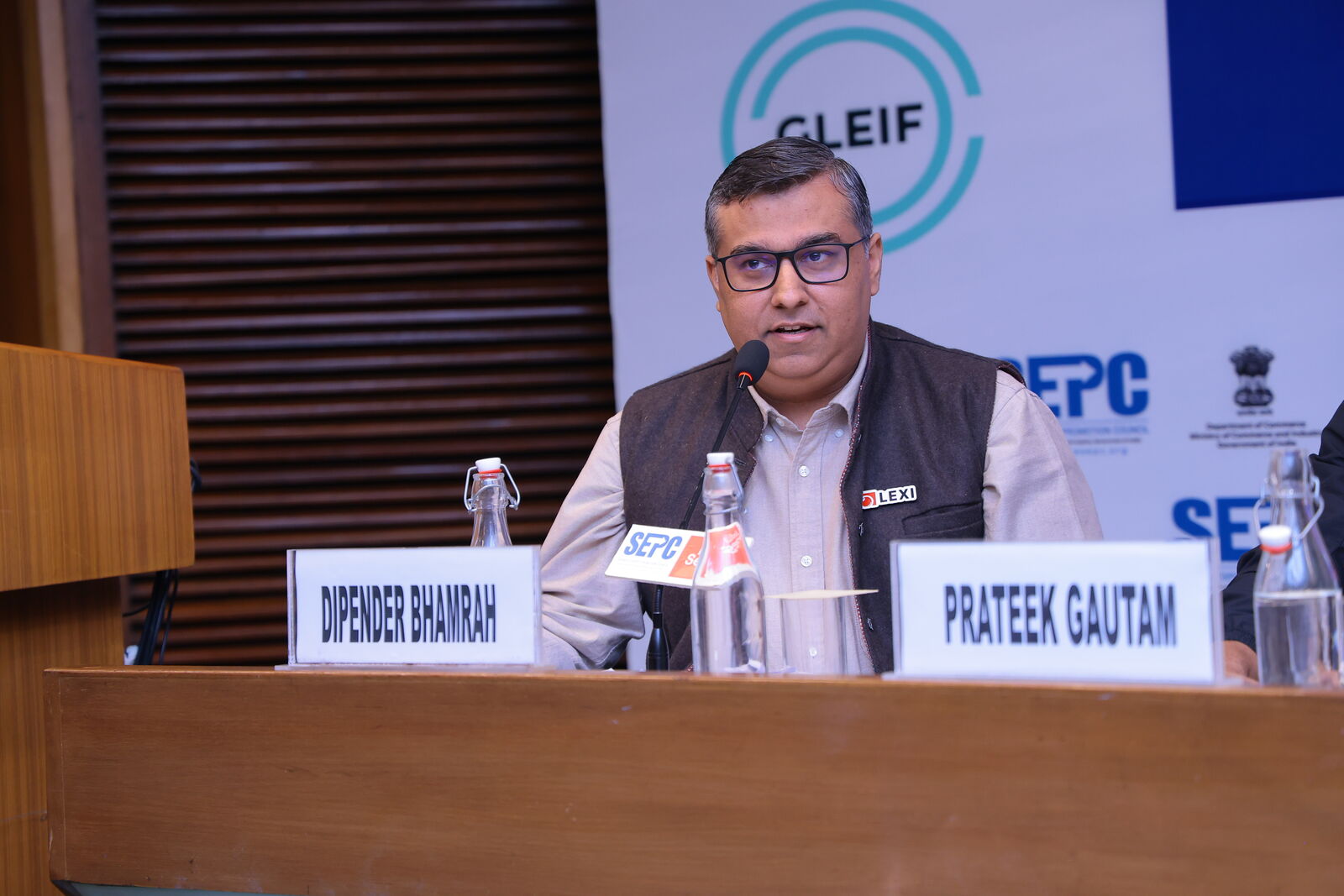 Dipender Bhamrah speaking at the Finolegal Convergence Summit 2025, his name card on the table in front of him